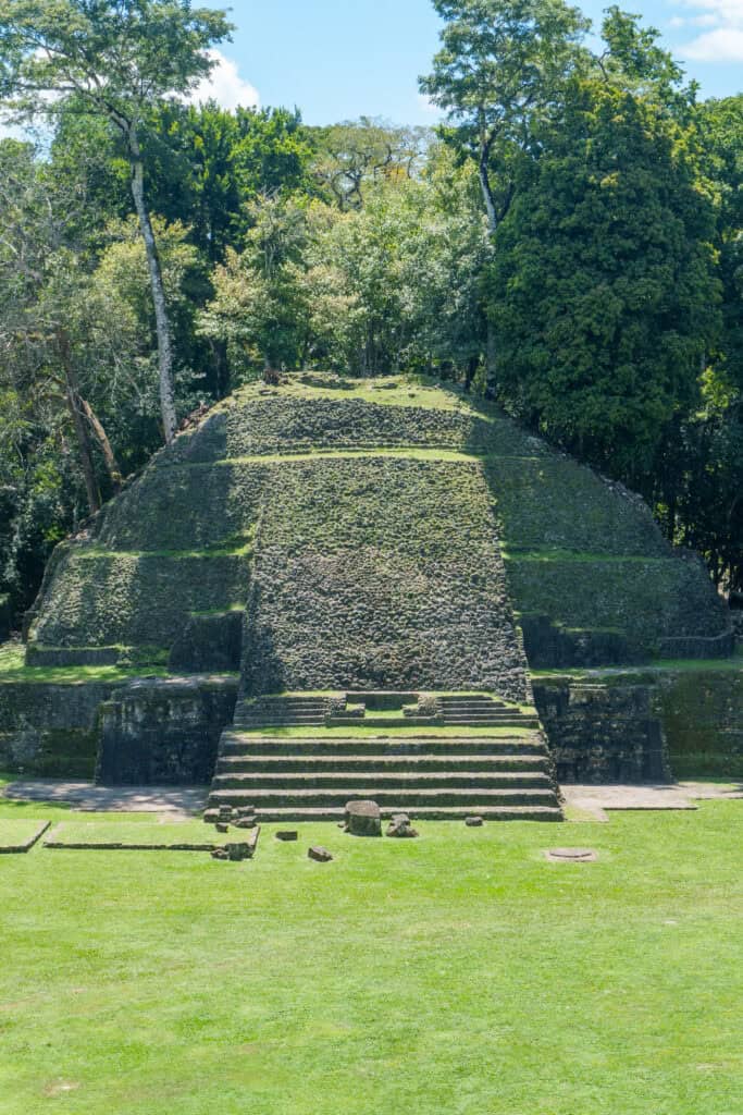 Ancient stone pyramid with staircases, a testament to the remarkable Maya civilization, surrounded by green grass and dense trees under a blue sky.