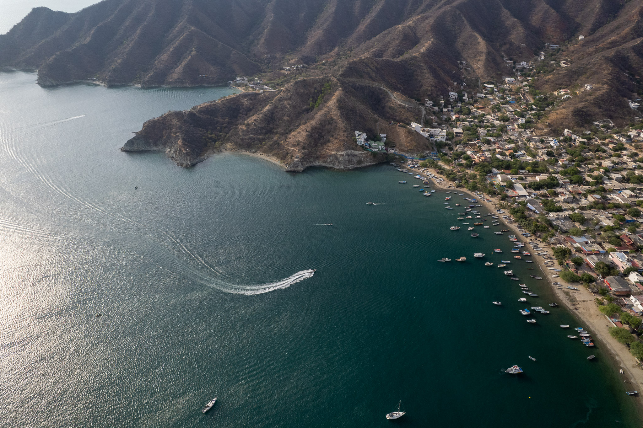 Aerial view of taganga bay with the village and the sea with boats near the beach. one boat is cruising back to the beach.
