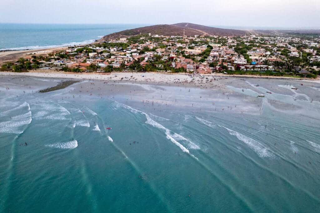 Aerial view of Jericoacoara at sunset. there are many people in the sea and on the beach enjoying the view of the sunset. we see the city behind the beach.