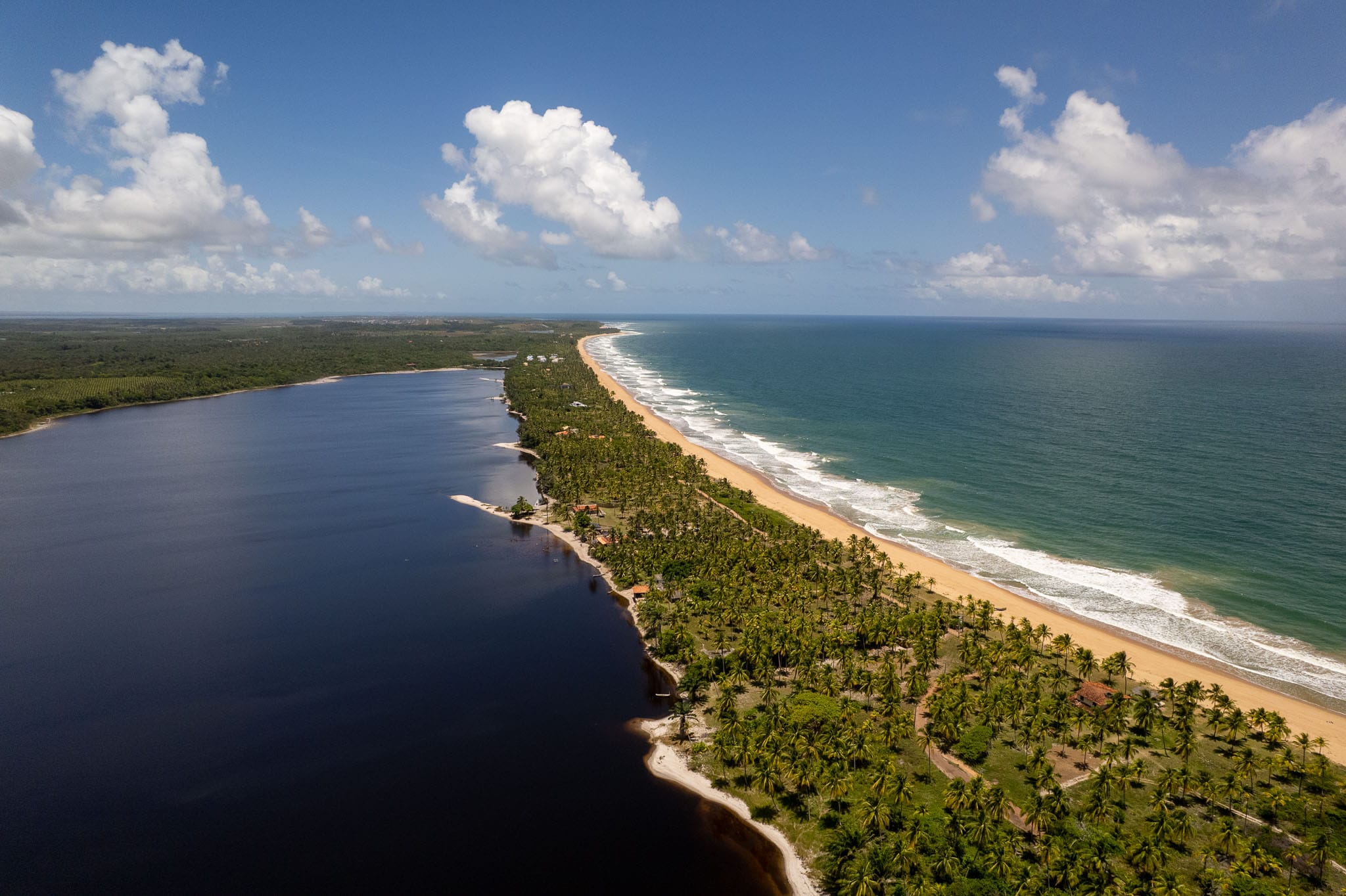 Aerial view of 'lagoa do cassange' and 'praia do cassange' at the peninsula of Marau, in Brazil. the lake is dark blue, there is palm trees, the beach and then the turqoise sea.