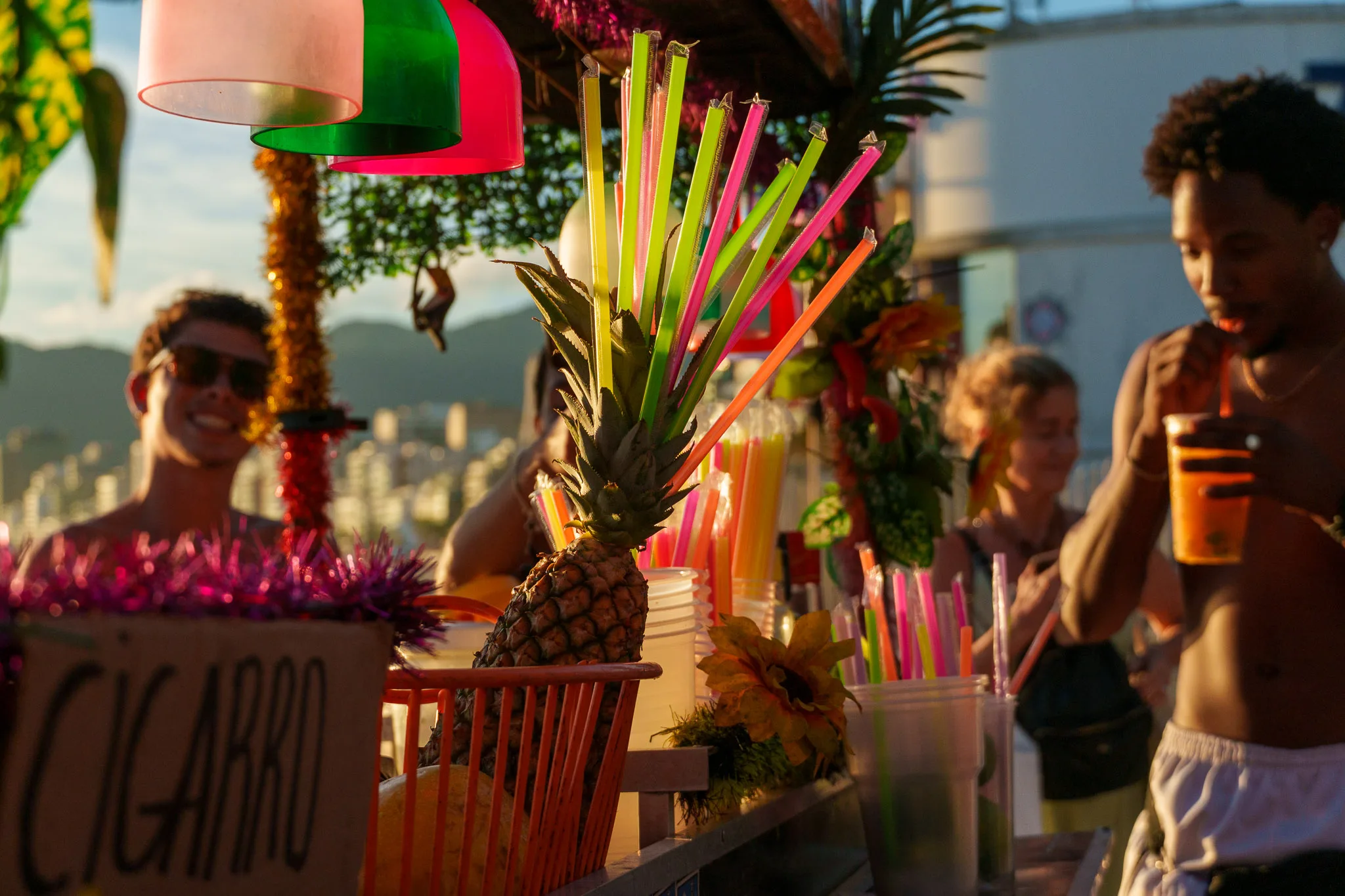 mobile shop of caipirinha at arpoador in Ipanema during the sunset. there is a pineapple with straw on the foreground.