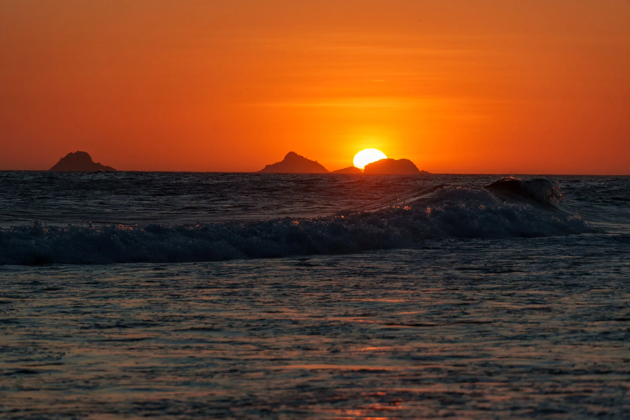 Sunset with waves and yellow orange sun at Ipanema beach in Rio de Janeiro, Brazil.