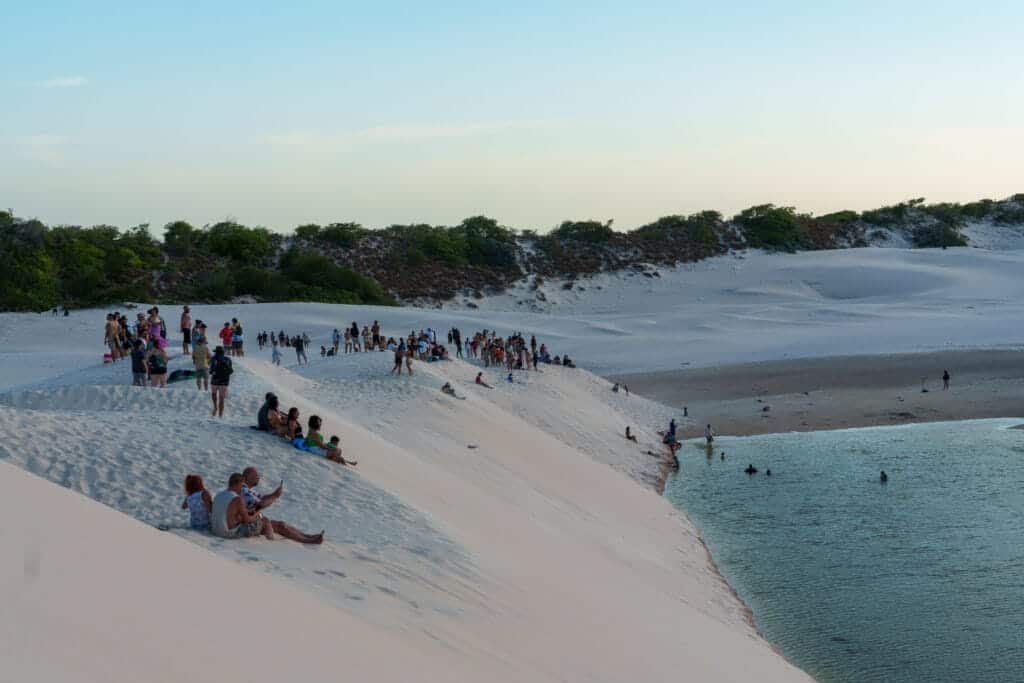 people watching the sunset at Lencois Maranhenses national park. they are sitting on the dune above the lagoon.