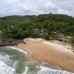Aerial view of the Tiririca beach near the town of Itacaré, Brazil. the sea meets the jungle, the ebach is small with parasol, chairs and people.