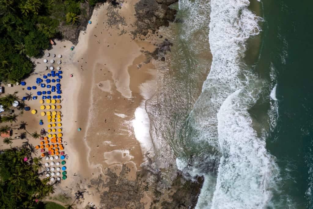 aerial view of praia resende in Itacaré, Brazil. various restaurant have parasol of different colors, the beach is empty, and there are waves.