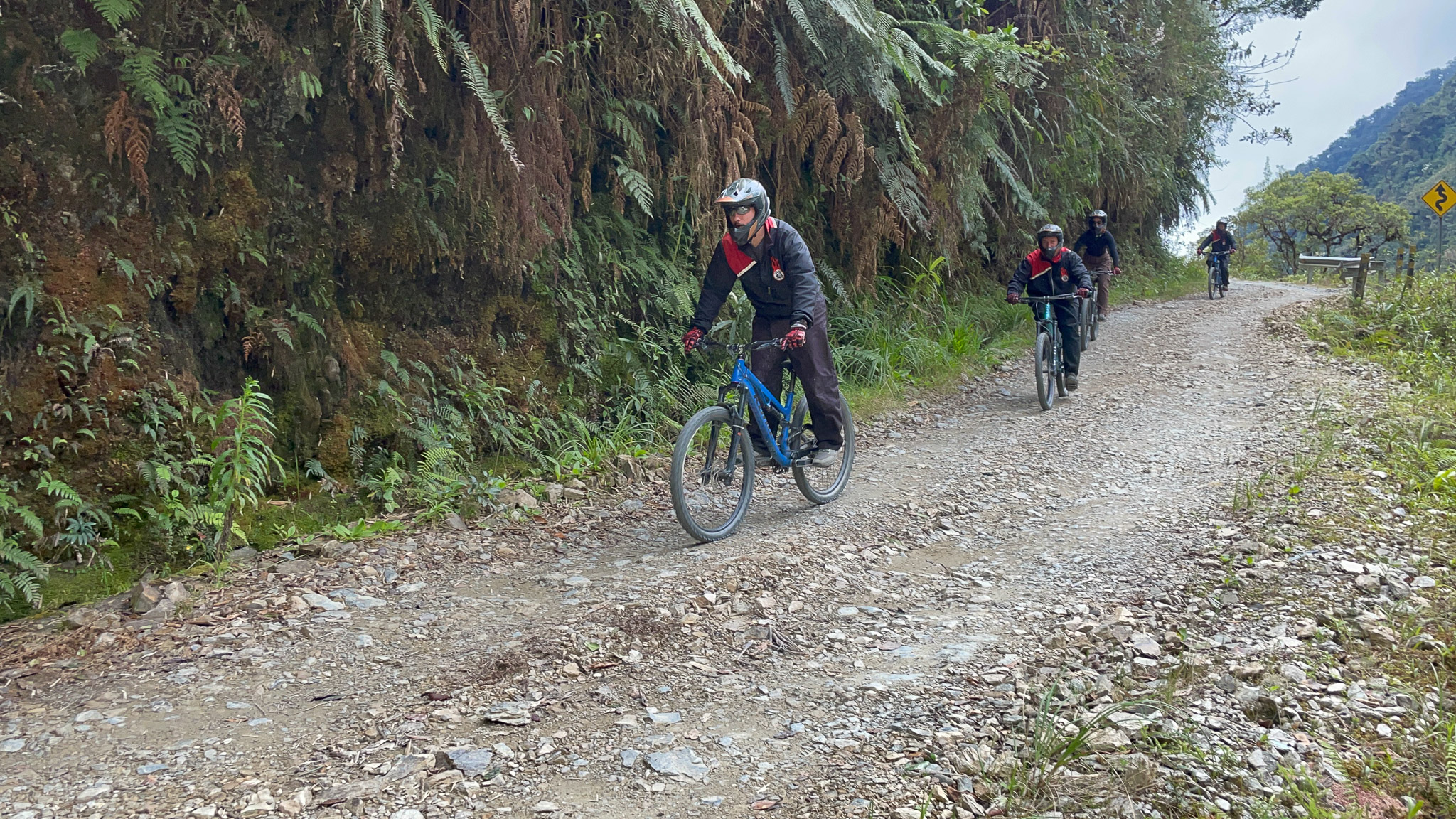 People riding bike with Gravity Bolivia riding down the Death Road. 4 people are following each other, with full equipment on them.