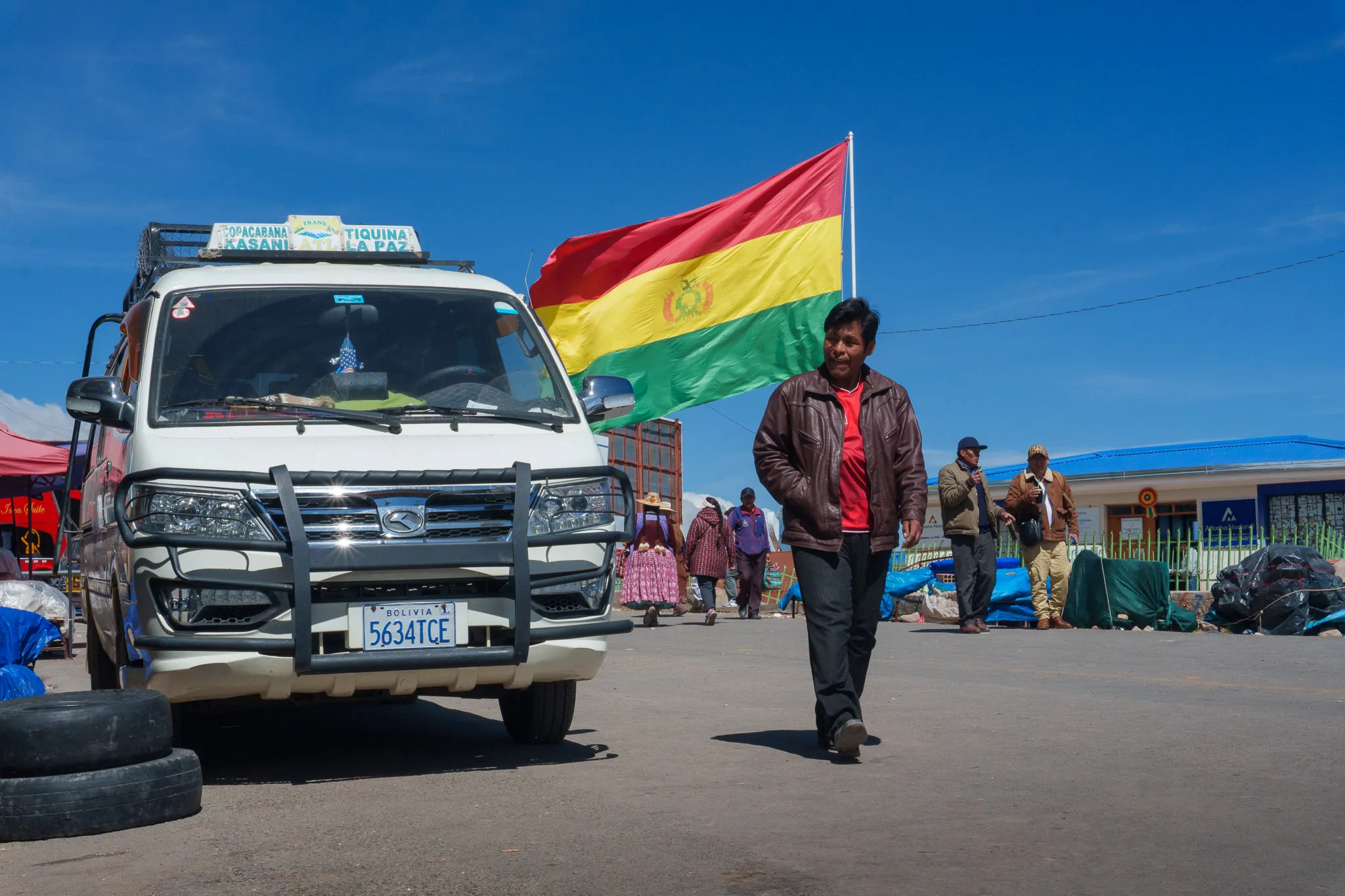 Man walking next to van in Bolivia. in the background there is the Bolivian Flag.