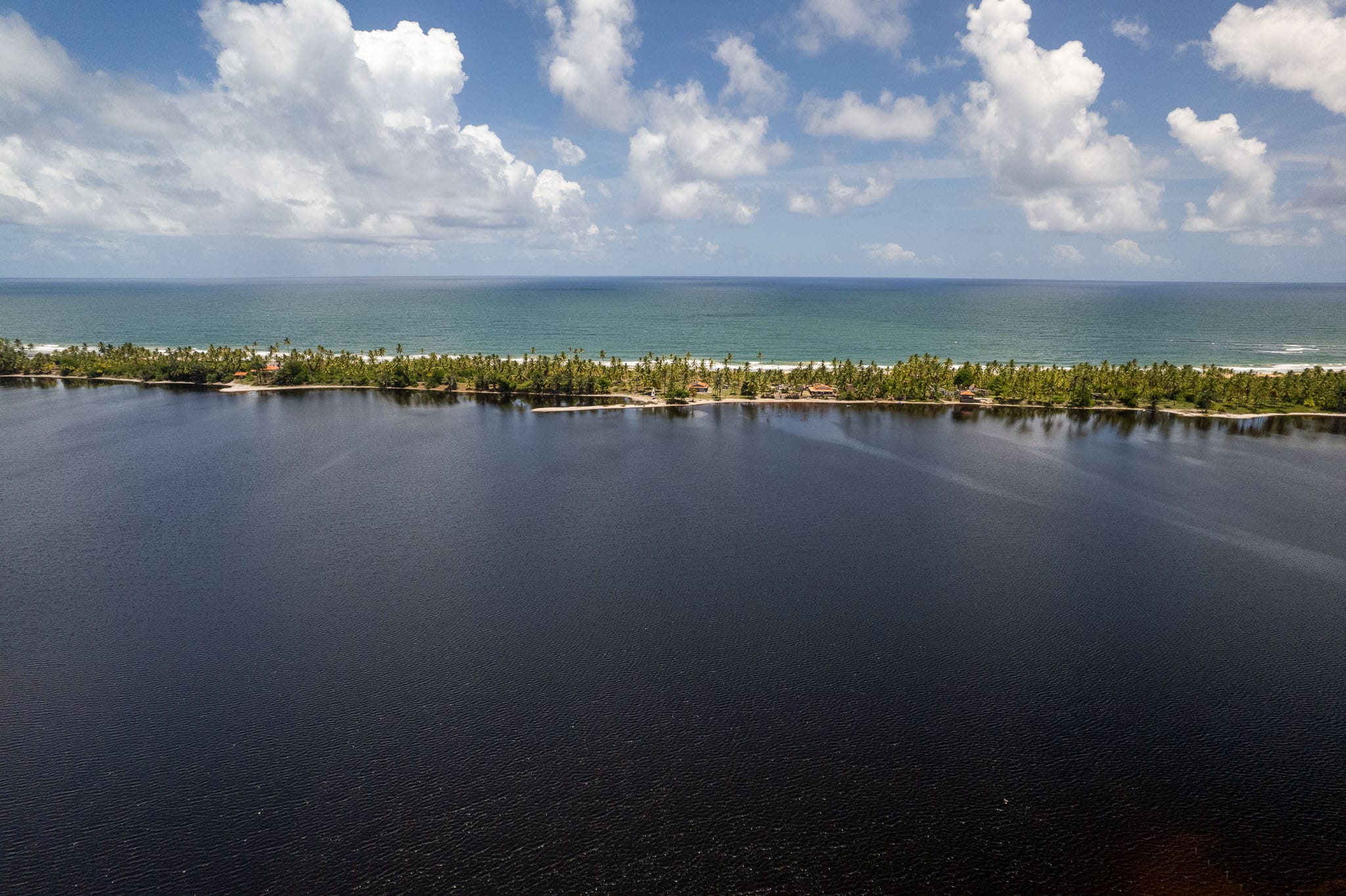 aerial view of taipu da fora beach and lagoa do cassange at the marau peninsula in Bahia region, Brazil. the lake is dark blue while the sea is turquoise.