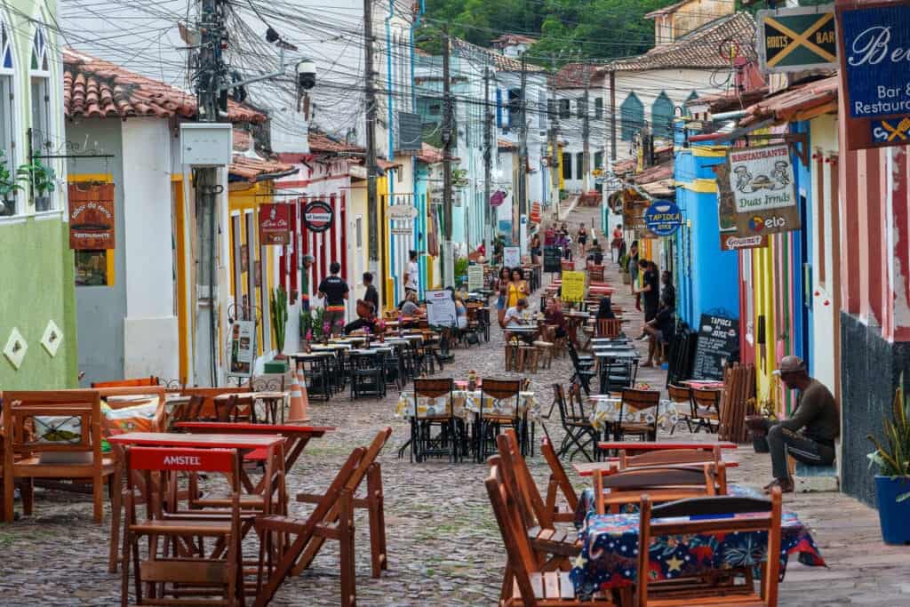Street in LEncois Bahia. There are tables fromr restaurants, houses and walls are colorful, people are outside walking in the street.