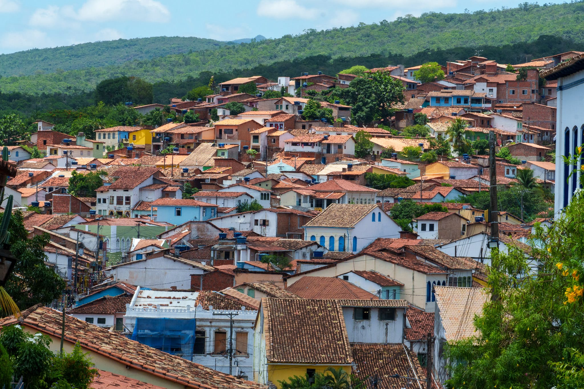 compressed view of houses of lencois in Bahia, Brazil. houses have red tiles and colorful walls. the city is surrounded by forest.