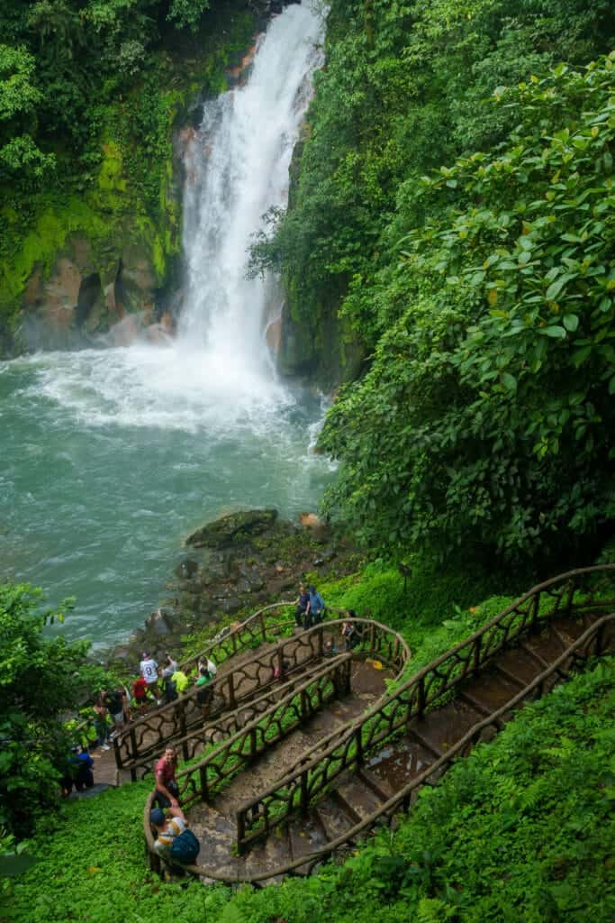 wide view of the waterfall and celeste river with the stairs to go down, national park of volcan tenorio, costa rica.