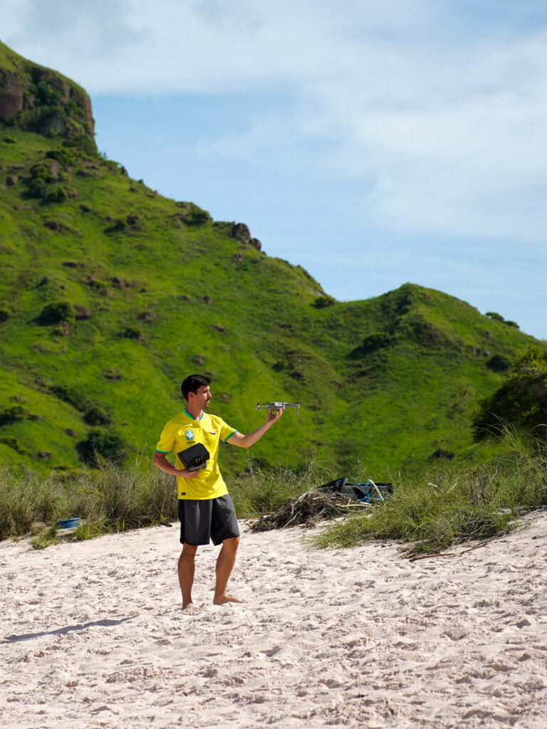 me ( horizonhugo) flying a drone on a pink beach at padar island, with agreen hill behind me