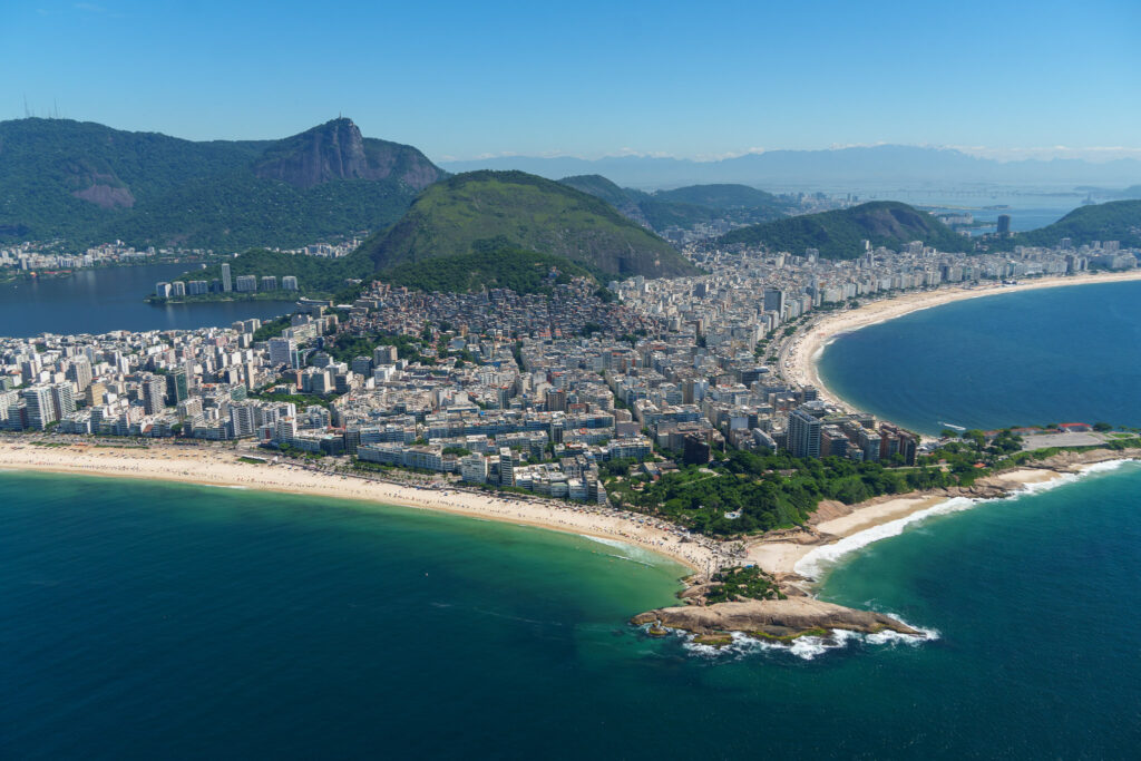 Aerial view of Rio de Janeiro showing Copacabana Beach, city buildings, lush green hills, and blue ocean under a clear sky—discover breathtaking scenes like this on a helicopter tour Rio de Janeiro offers at an unbeatable price.