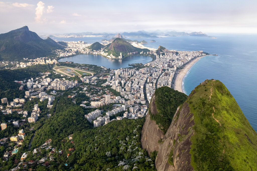 Aerial view of Rio de Janeiro showing lush mountains, urban buildings, sandy beaches, and ocean under a cloudy sky, with the iconic Morro Dois Irmãos rising prominently—a popular destination for those seeking the best hike in Rio.